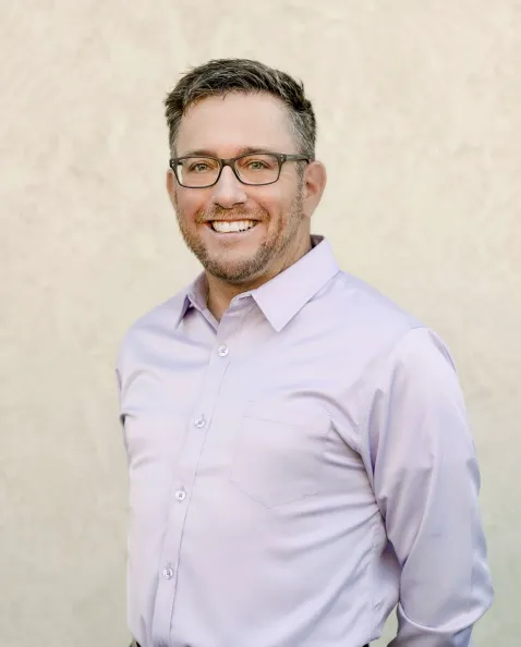 A man in glasses and a shirt smiling for the camera.