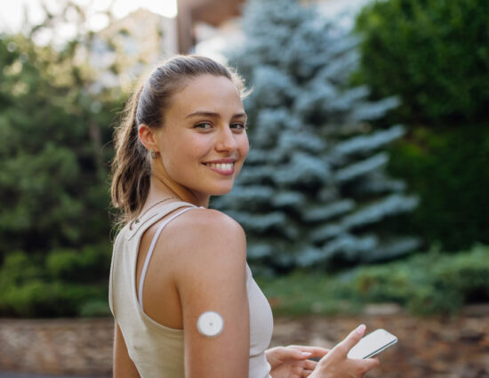 Beautiful diabetic woman preparing for outdoor workout in the city. Young woman with CGM checking her blood sugar level before exercising. Concept of exercise and diabetes.